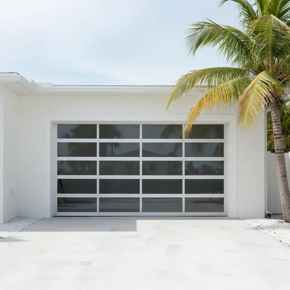 Newly installed modern glass and aluminum garage door reflects blue sky on a stucco home in Hallandale Beach.