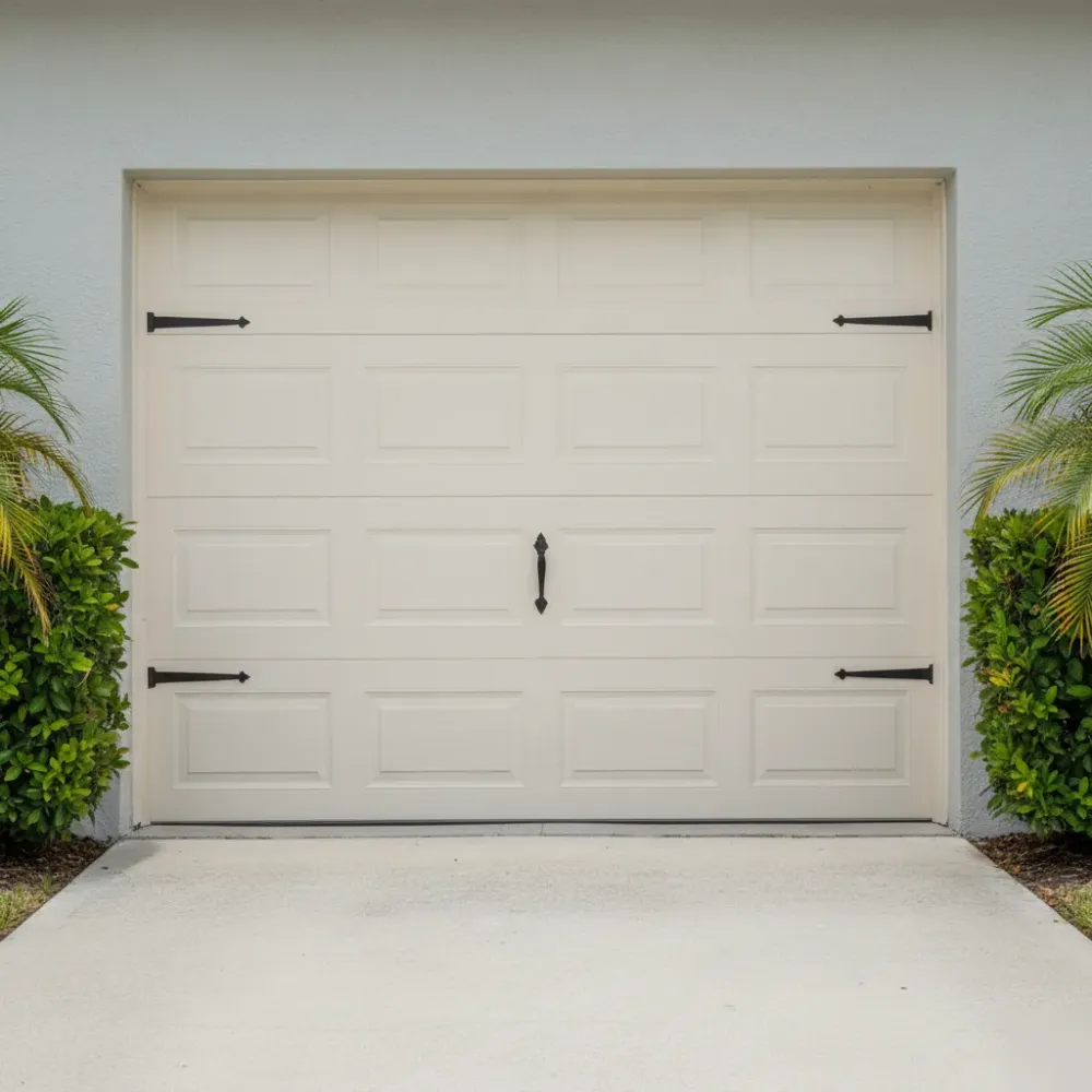 Finished white raised-panel garage door with bronze strap hardware on a pale gray stucco home exterior.