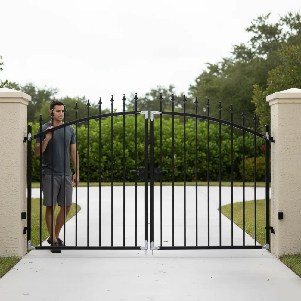 Person rests a hand on a freshly repaired black wrought iron swing gate with new silver hinges on a clean concrete driveway.